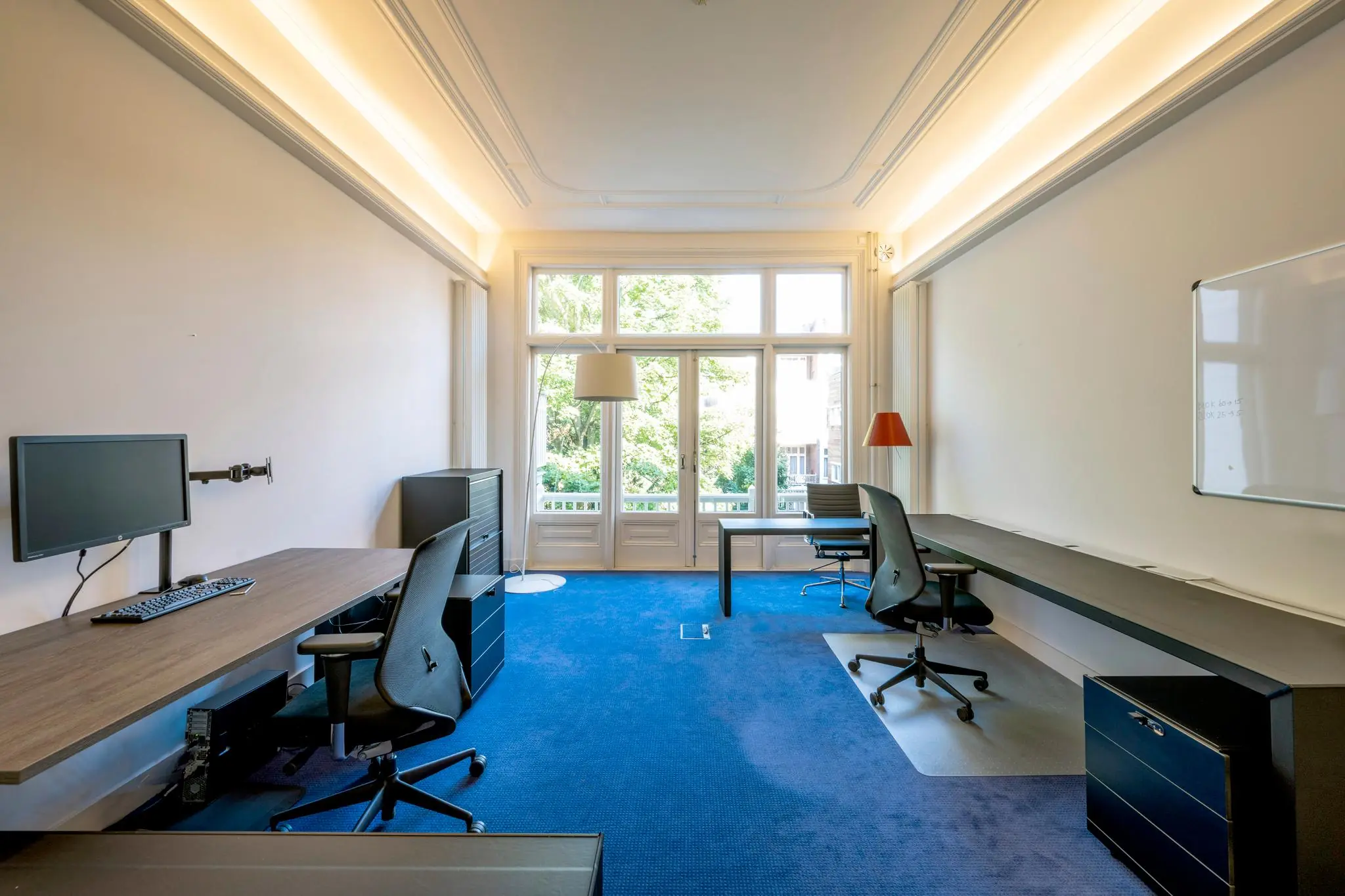 Modern kantoor aan de Paulus Potterstraat met twee werkplekken, grote ramen en blauwe vloerbedekking.